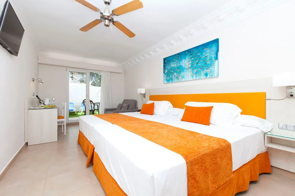Dormitorio moderno con cama blanca y naranja, ventilador y cuadro azul en pared
