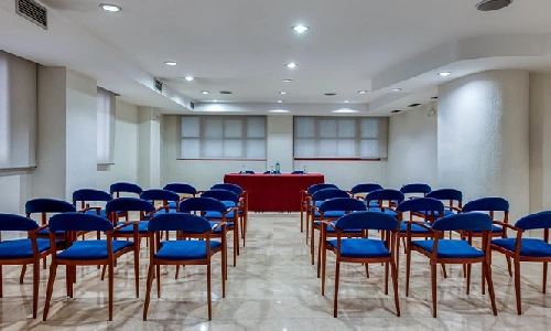 Sala de conferencias vac&iacute;a con sillas azules y una mesa al frente.
