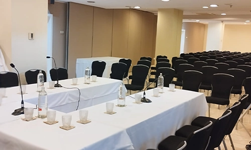 Sala de conferencias vac&iacute;a con mesas blancas y sillas negras.