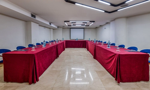 Sala de conferencias con mesas en U y sillas azules.