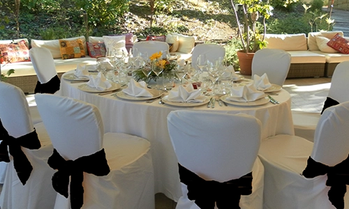 Mesa de banquete con sillas blancas decoradas y un centro de flores.