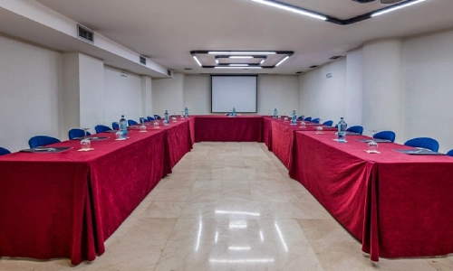 Sala de reuniones con mesas en U y sillas azules, preparada para conferencia.