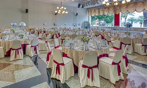 Sal&oacute;n de bodas elegante con mesas decoradas y sillas con lazos rojos.