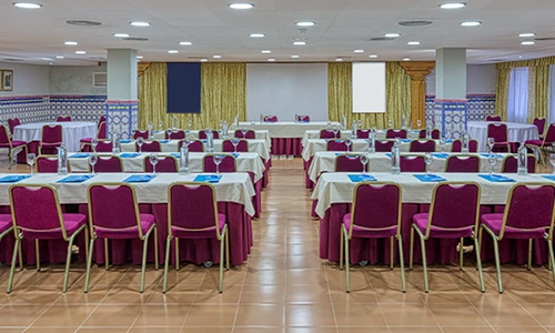 Sala de conferencias con mesas y sillas dispuestas en hileras.