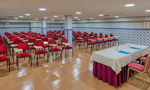 Sala de conferencias vac&iacute;a con sillas rojas y mesas con manteles blancos.