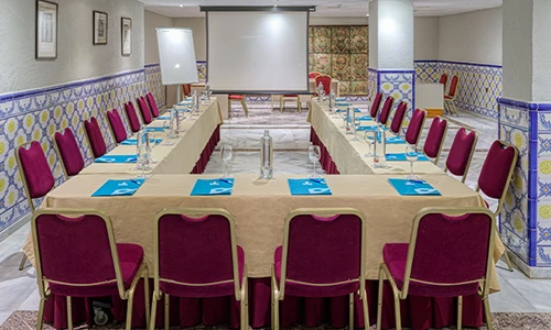 Sala de reuniones en forma de U con sillas rojas y mesas cubiertas con manteles.