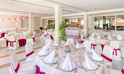 Sal&oacute;n de banquete decorado con manteles y sillas en tonos blancos y rosas.