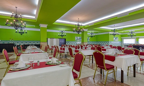Comedor elegante con paredes verdes, mesas y sillas rojas con manteles blancos.