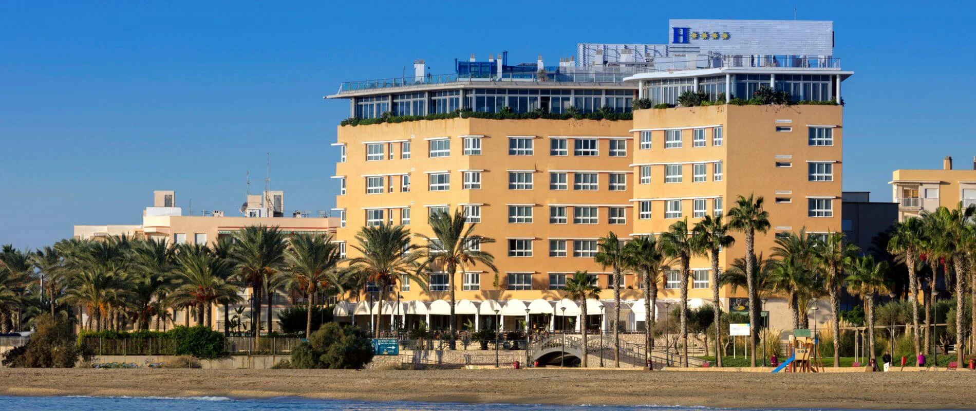 Hotel frente al mar, edificio naranja con palmeras y cielo azul