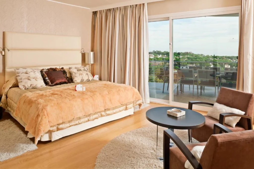 Dormitorio con cama y sala junto a terraza con vista al jard&iacute;n