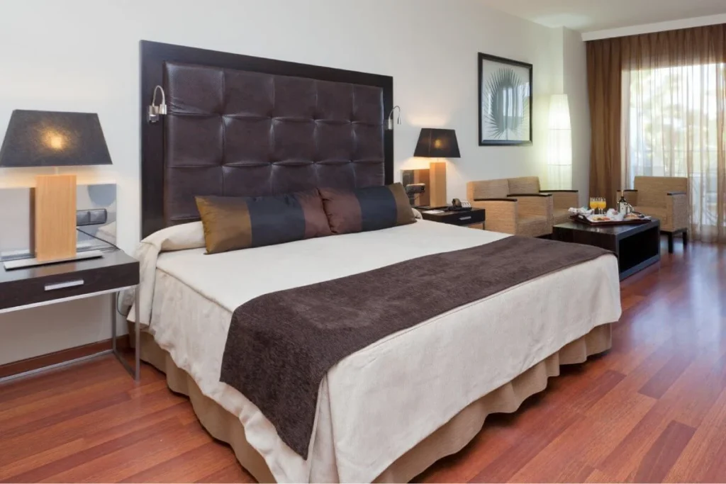 Habitaci&oacute;n de hotel moderna con cama doble, mesitas y cortinas.