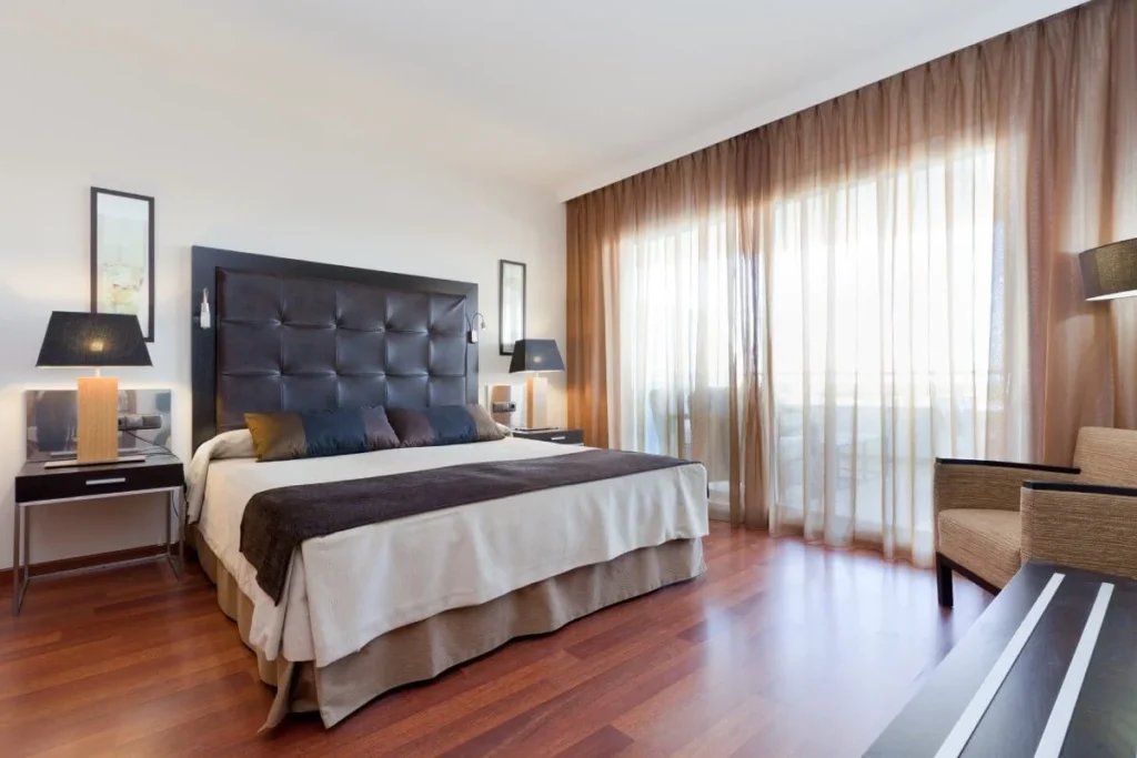Dormitorio moderno con cama, l&aacute;mparas y cortinas junto a la ventana.