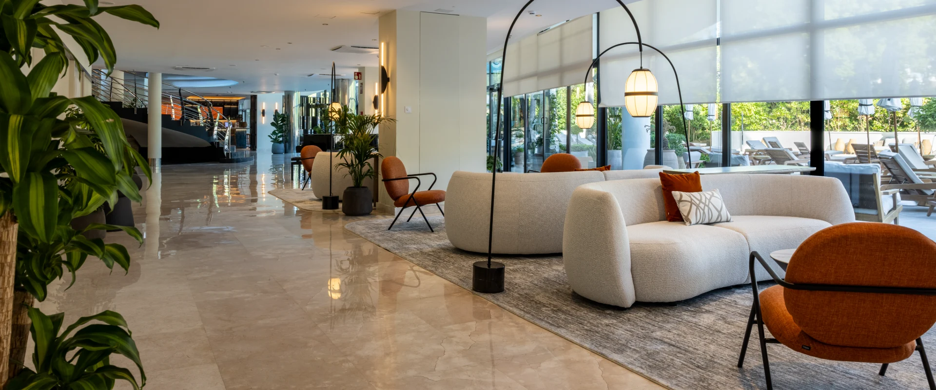 Lobby moderno con sof&aacute; beige, l&aacute;mparas colgantes y ventanales con luz natural