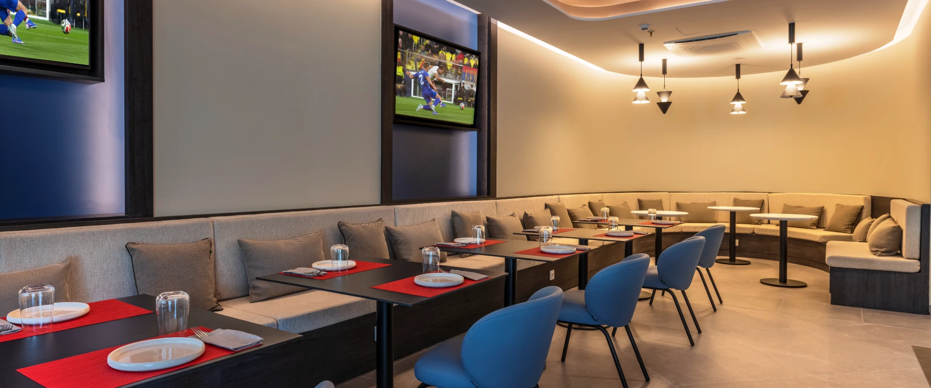 Sala de restaurante con mesas, asientos y pantallas con f&uacute;tbol.