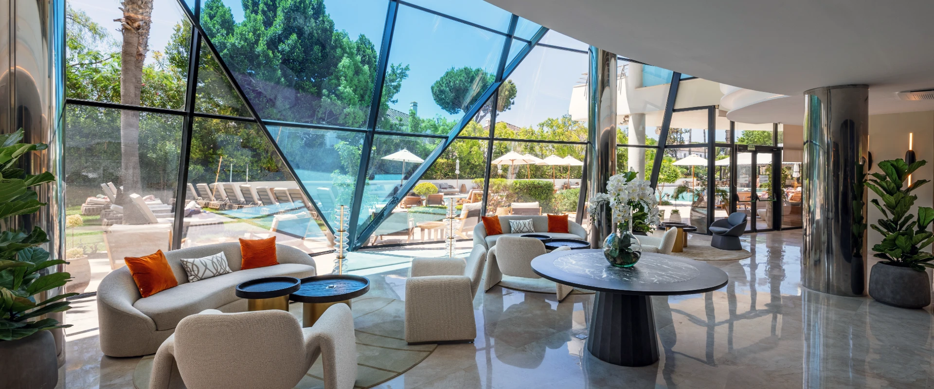 Sala moderna con vista a piscina, palmeras y mobiliario de exterior.