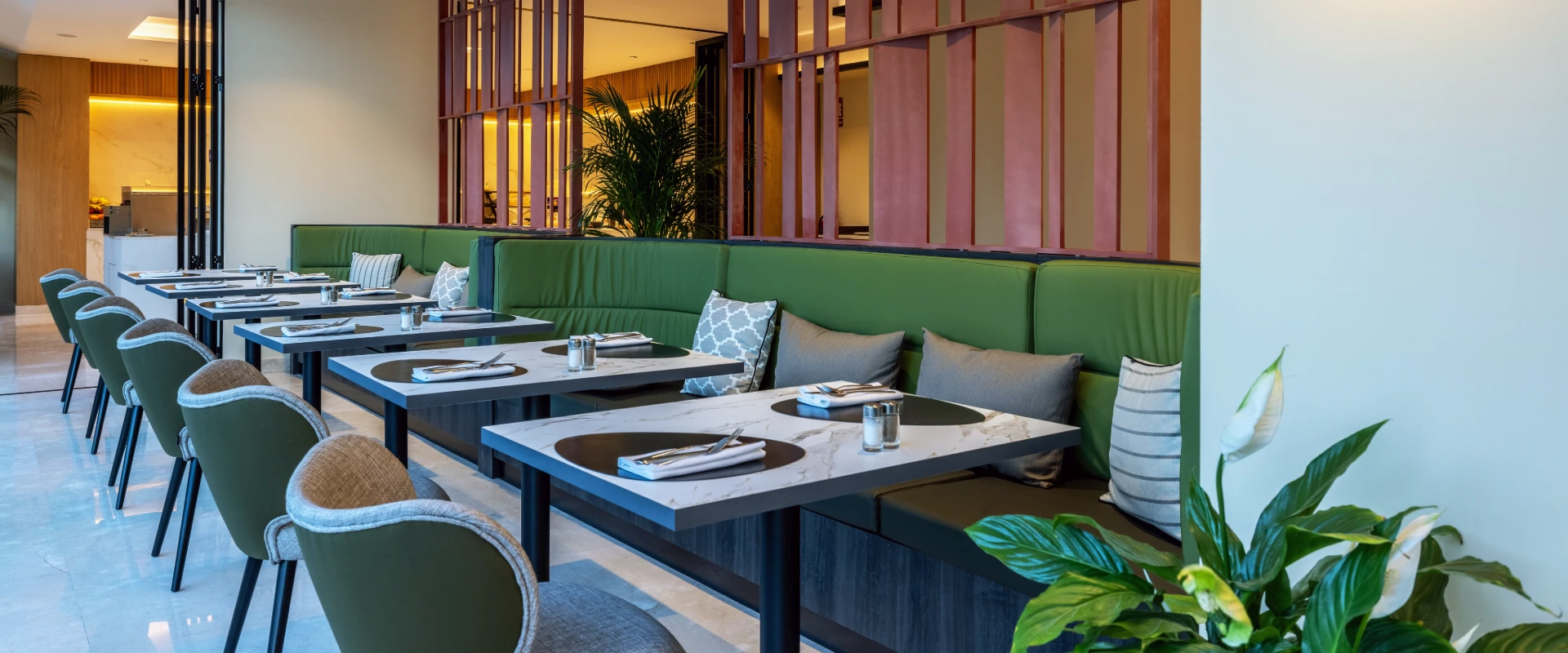 Restaurante con mesas y sof&aacute;s verdes, iluminaci&oacute;n c&aacute;lida y palmeras al fondo