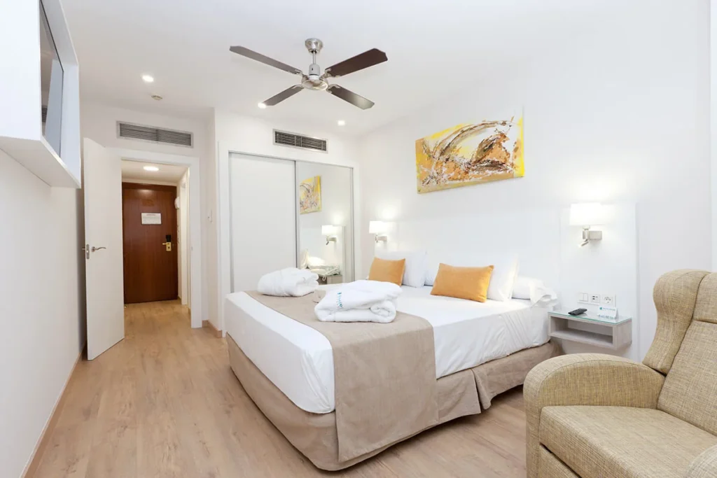 Dormitorio moderno con cama doble, sill&oacute;n y ventilador de techo, luz blanca