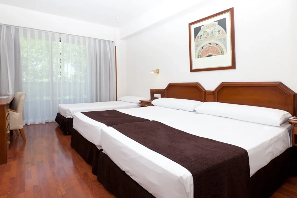 Habitaci&oacute;n con dos camas dobles, cortinas y cuadro en pared blanca