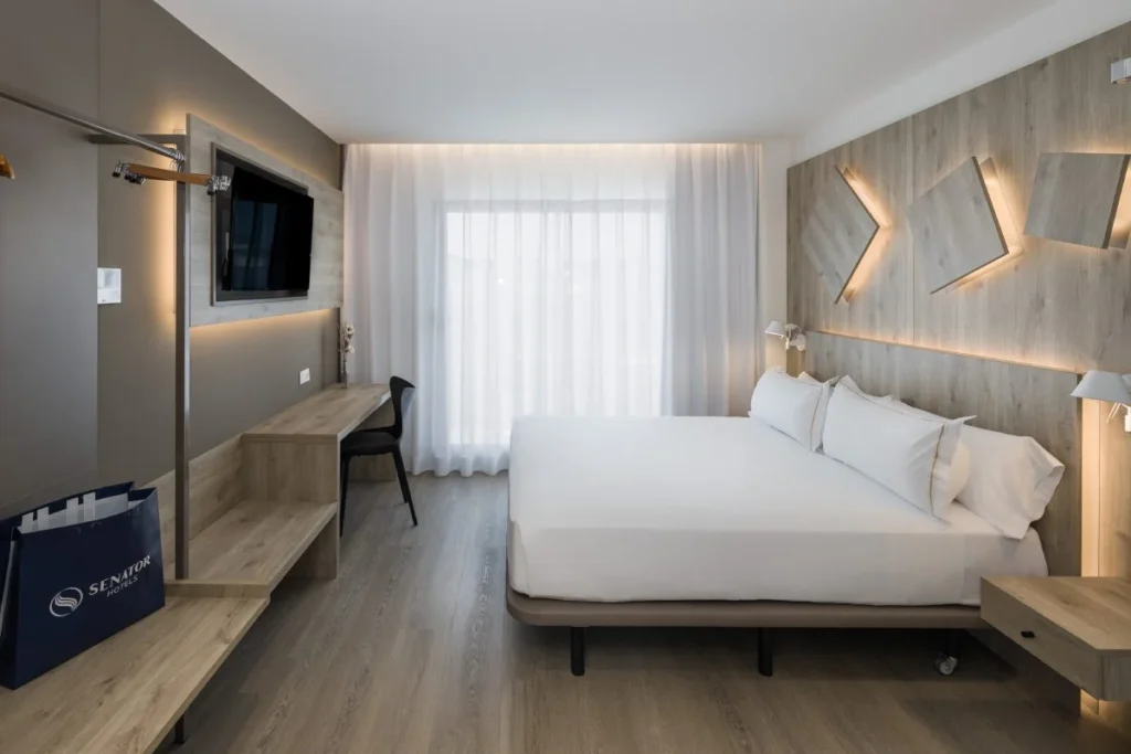 Habitaci&oacute;n de hotel moderna con cama doble, escritorio y l&aacute;mparas LED