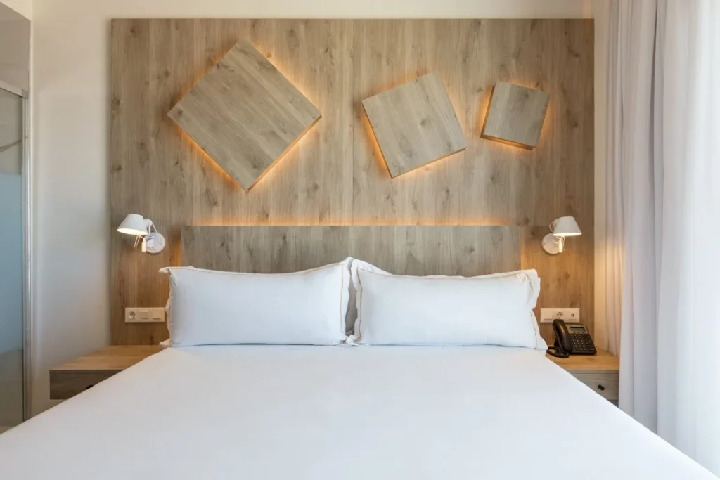 Dormitorio moderno con cama blanca, luces y panel de madera con cuadros iluminados.