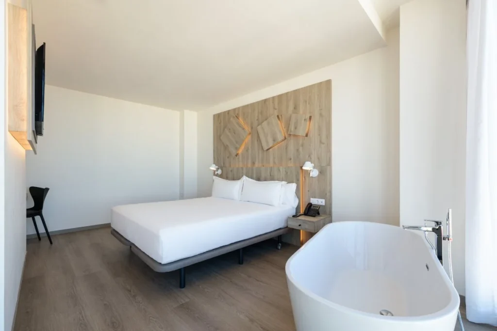 Habitaci&oacute;n de hotel moderna con cama blanca y ba&ntilde;era oval en esquina