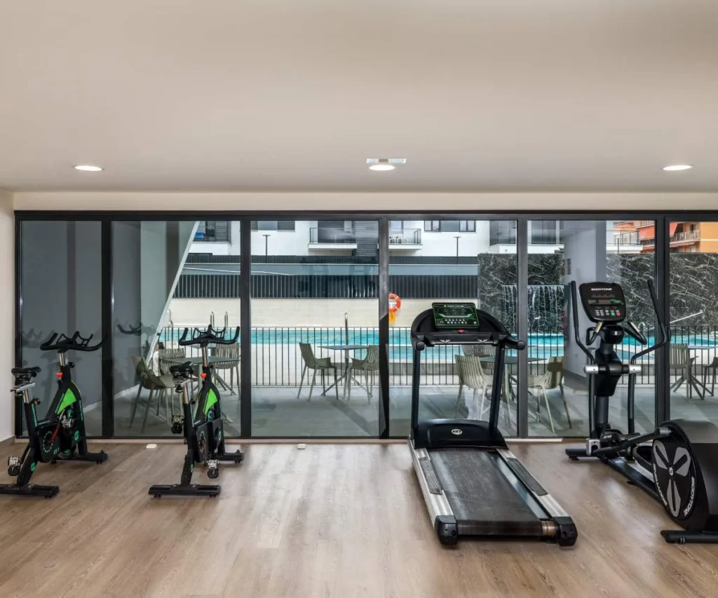Gimnasio con m&aacute;quinas de cardio y bicicletas, junto a ventanales al exterior