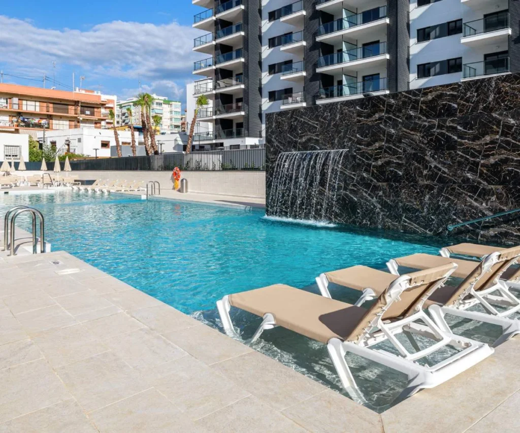 Piscina con hamacas y edificio moderno, vista al aire libre.
