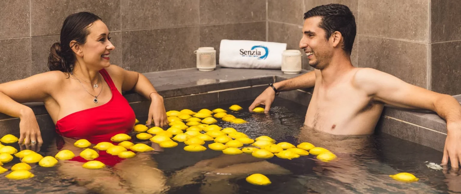 Pareja relaj&aacute;ndose en spa, con montones de p&eacute;talos de color amarillo en el agua
