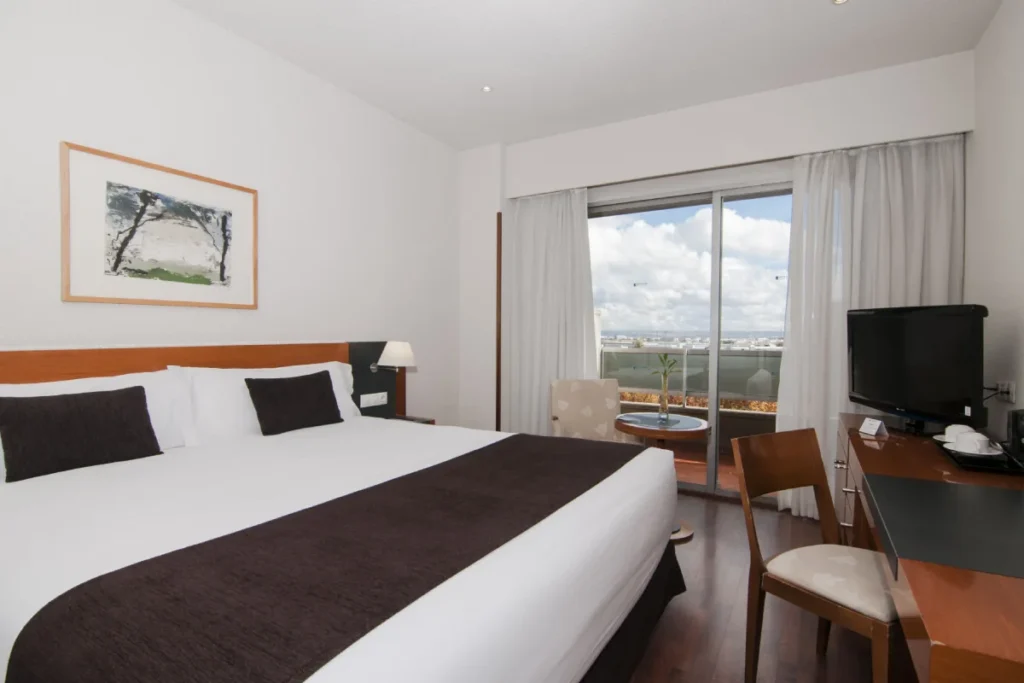 Habitaci&oacute;n de hotel moderna con cama, TV y vista por ventana grande