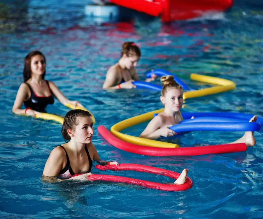 Ni&ntilde;os nadando en piscina con aros y flotadores de colores, con instructora