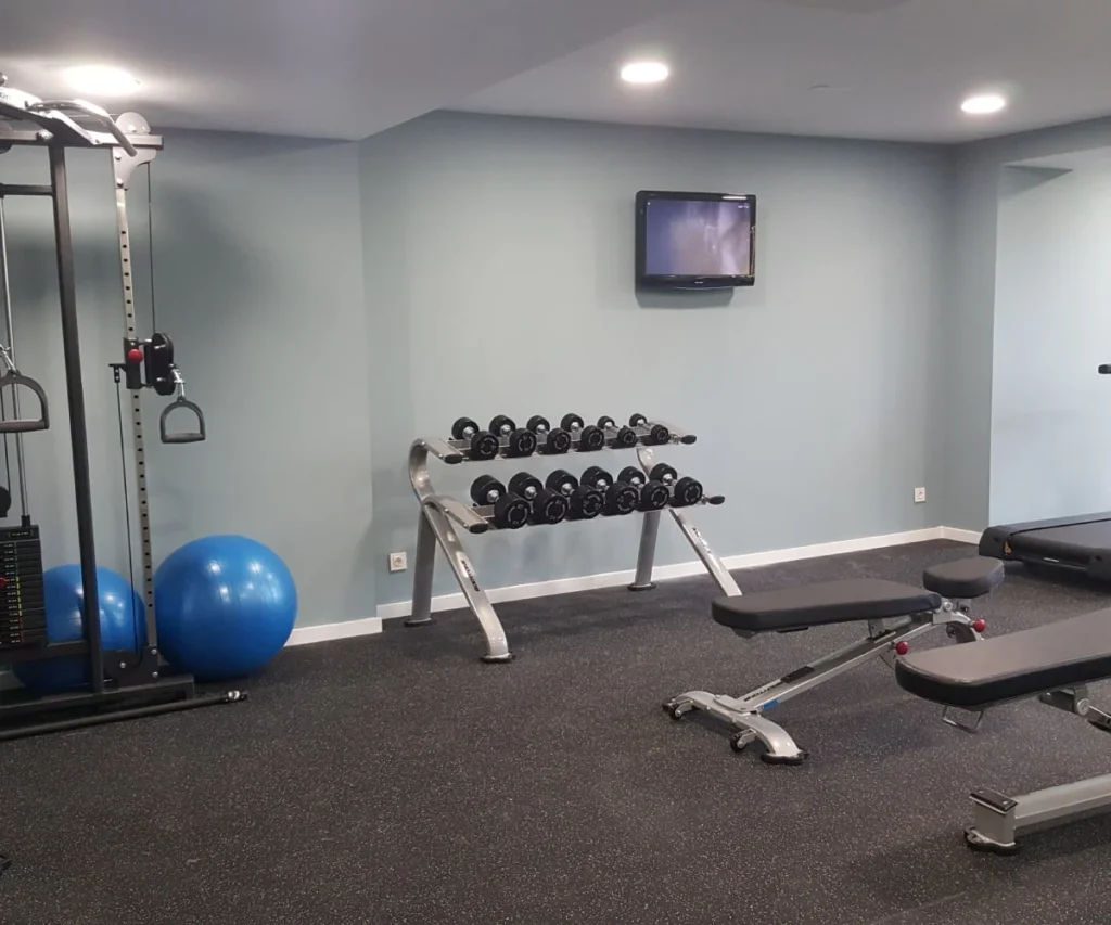 Sala de gimnasio con banco, mancuernas ajustables y TV en la pared
