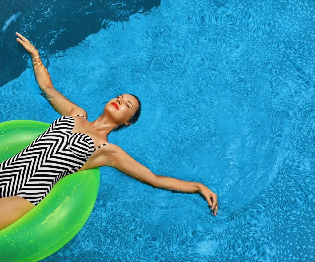 Mujer nadando en piscina con flotador verde, mirando al sol.