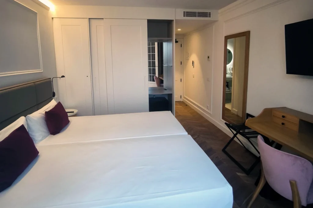 Habitaci&oacute;n moderna con cama doble, mesa, sillas y puerta a espejo.