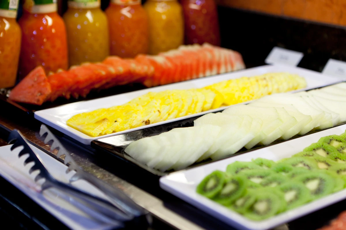Bandejas con frutas en rodajas: pi&ntilde;a, naranja, pepino, kiwi y mel&oacute;n, buffet.
