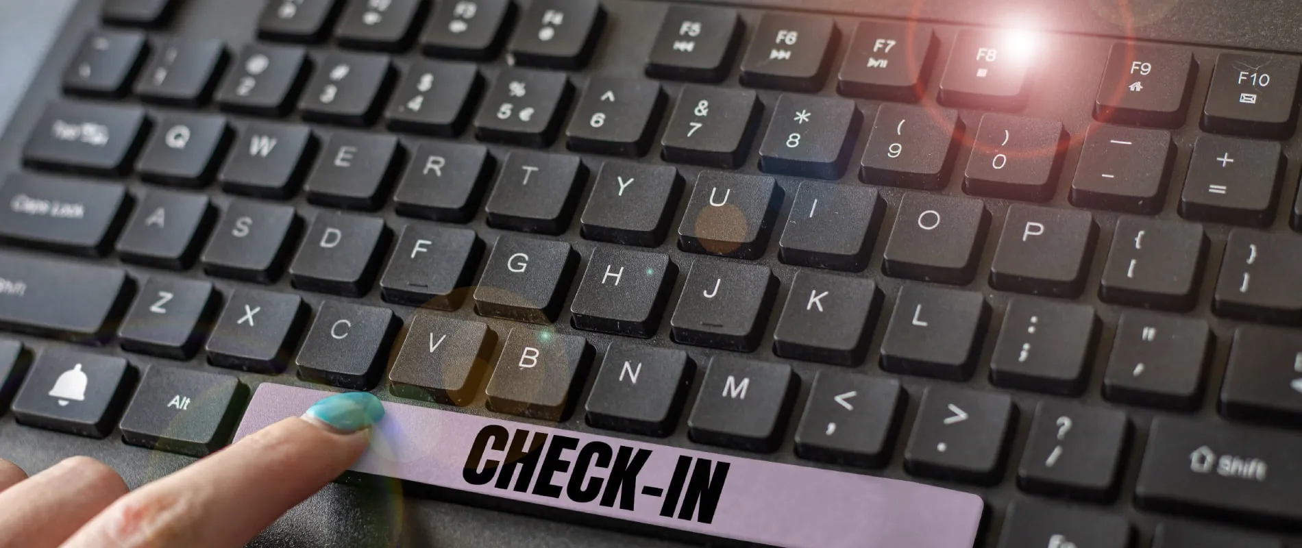 Teclado con luz y mano se&ntilde;alando tecla &ldquo;CHECK-IN&rdquo; en cinta morada