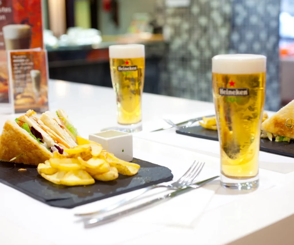 Dos vasos de cerveza y s&aacute;ndwich con papas fritas sobre mesa en un bar