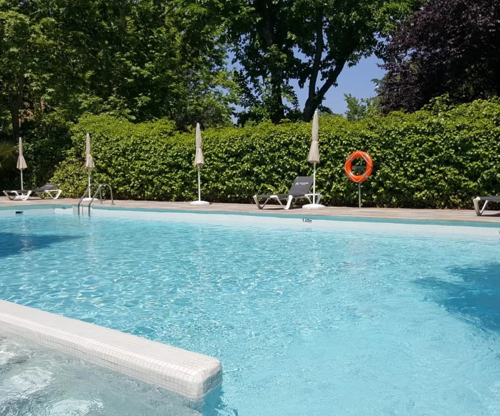 Piscina al aire libre con tumbonas, sombrillas y cercos verdes