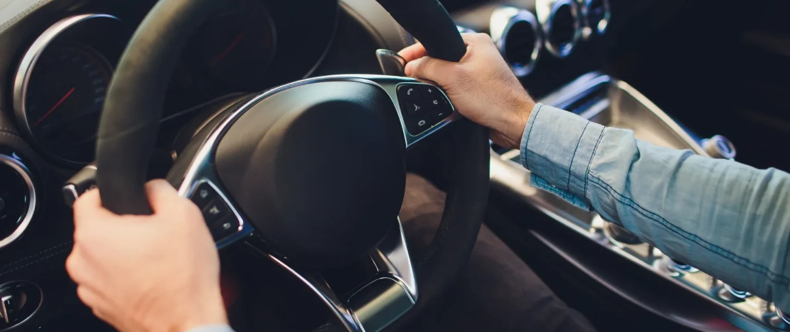 Manos en el volante y botones del coche, conduciendo en carretera