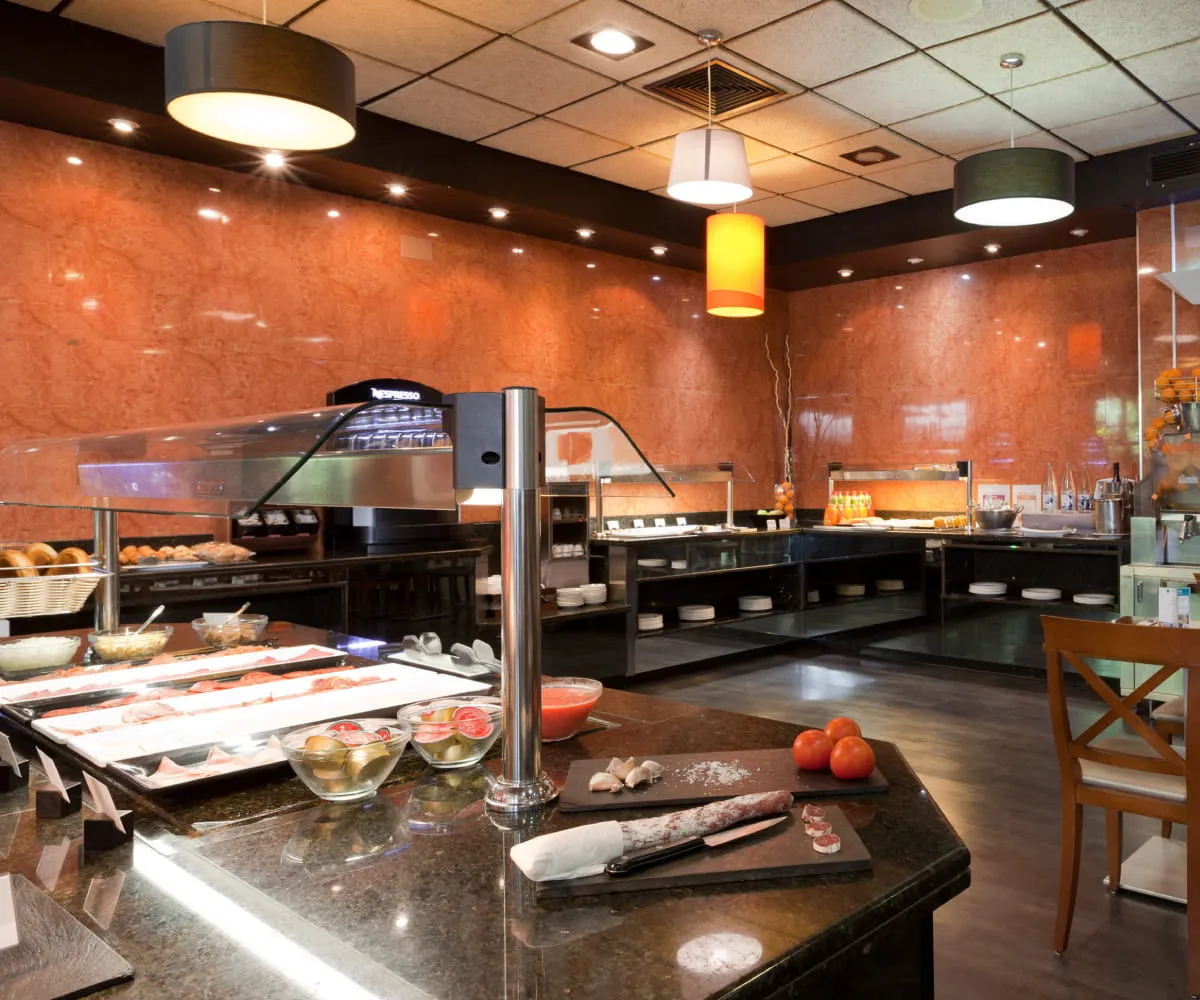 Cafeter&iacute;a buffet con m&aacute;quinas y barra de preparaci&oacute;n bajo luces colgantes