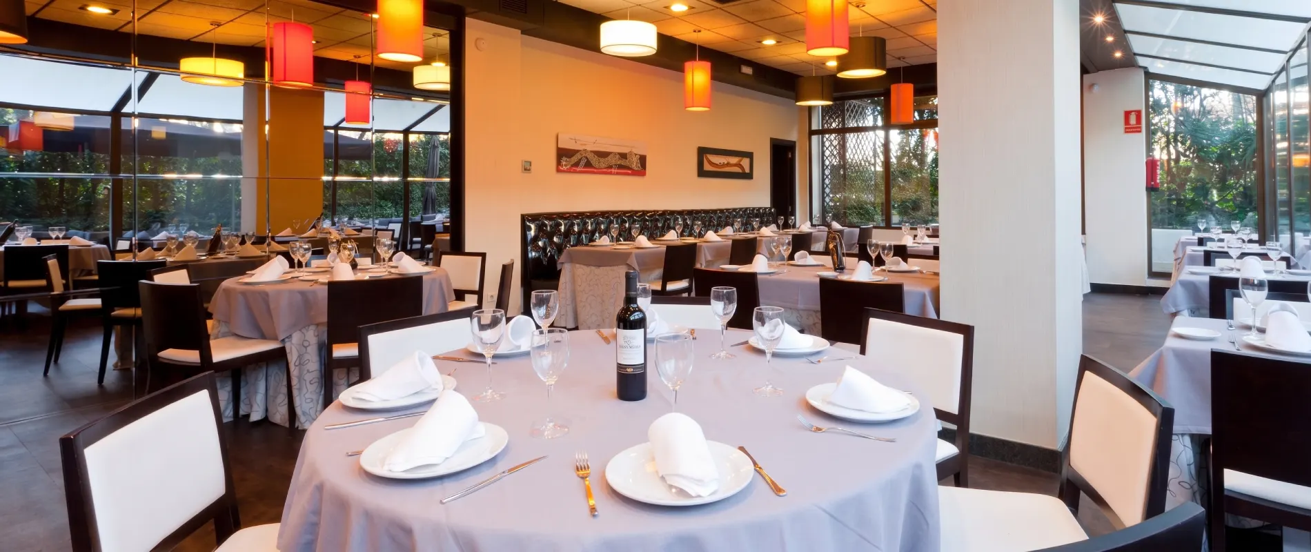 Comedor de restaurante con mesa puesta, copas y l&aacute;mparas naranjas.