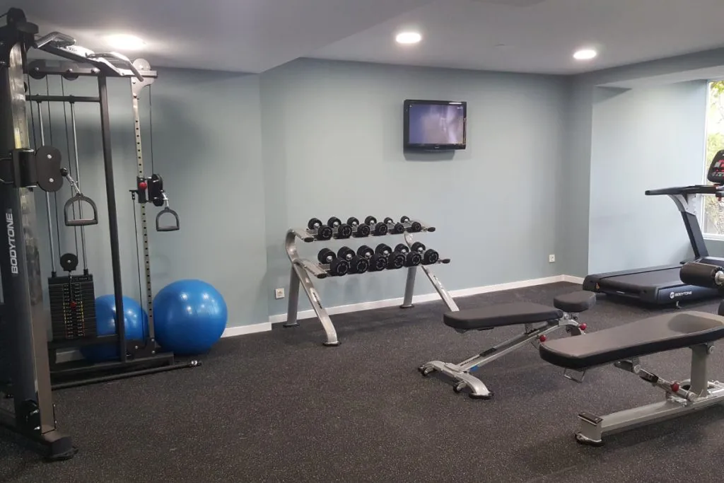 Gimnasio con pesas: estación de poleas, mancuernas, banco y caminadora.