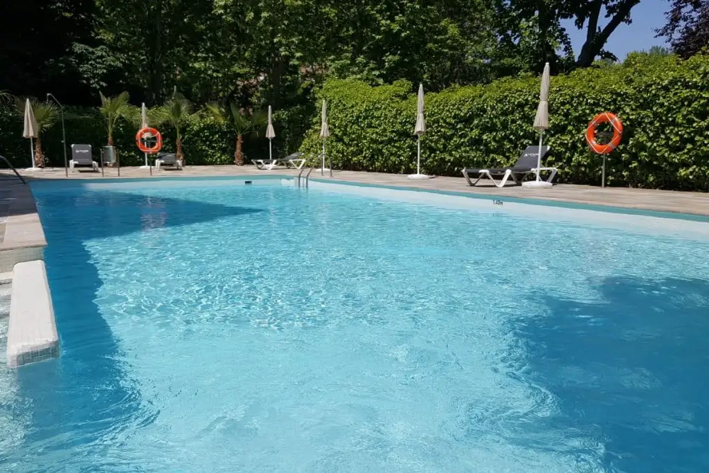 Piscina azul al aire libre con tumbonas, sombrillas y setos verdes