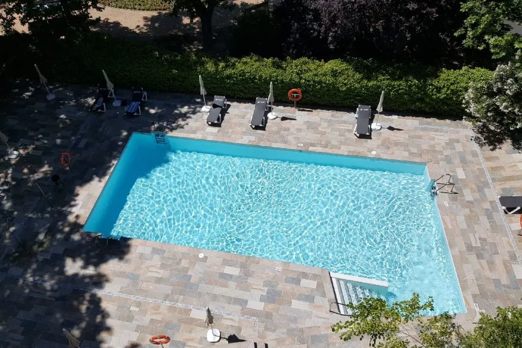 Piscina al aire libre con sillas y sombrillas en un jardín, vista cenital.