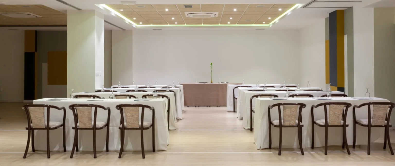 Sala de eventos con mesas servidas y sillas alrededor, al fondo decoraci&oacute;n floral
