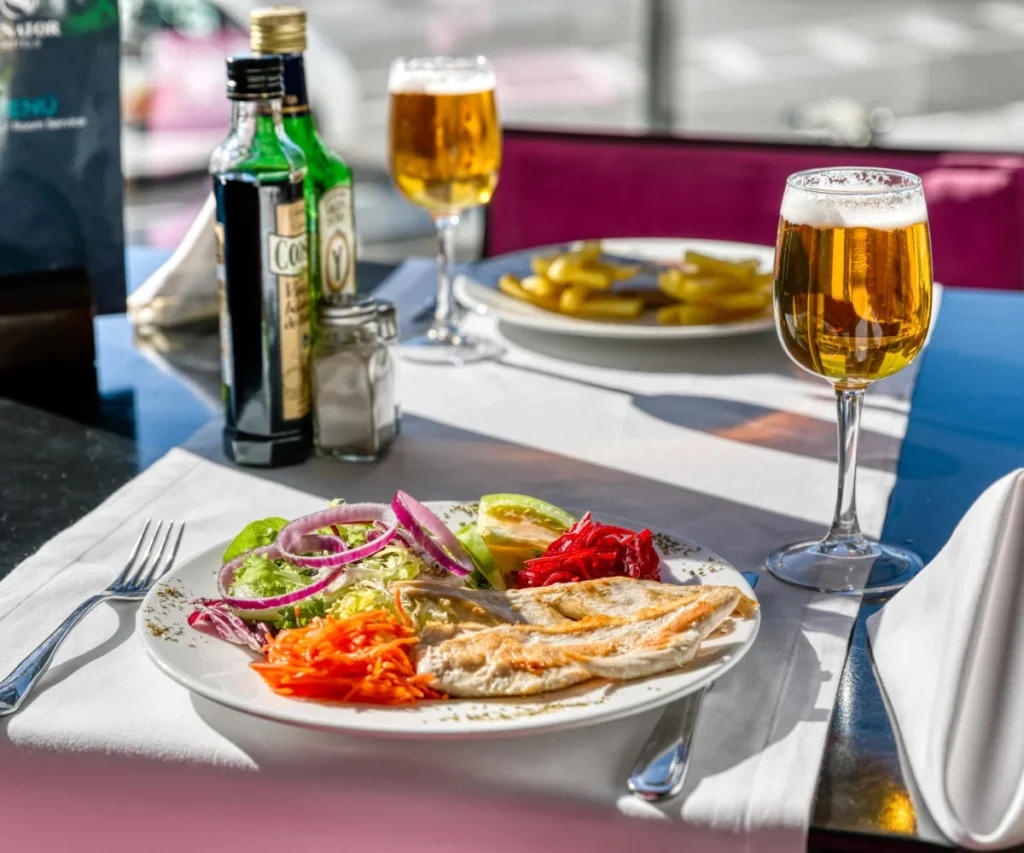 Plato con ensalada y cerveza en una mesa con botellas y vasos al sol