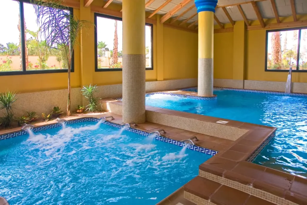 Piscina interior azul con columnas amarillas y azulejos decorativos.
