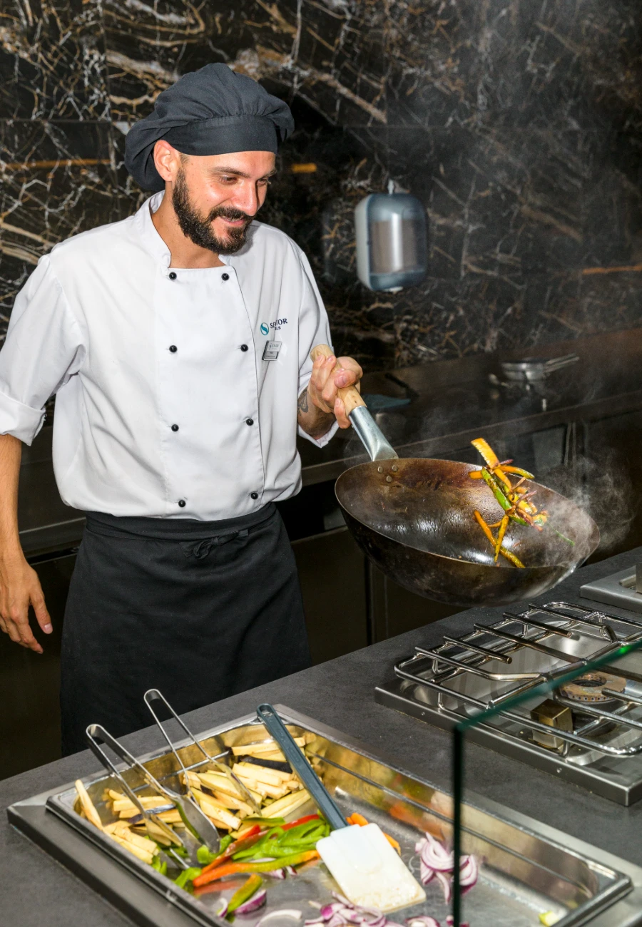 Chef cocinando salteado de vegetales en una cocina industrial.