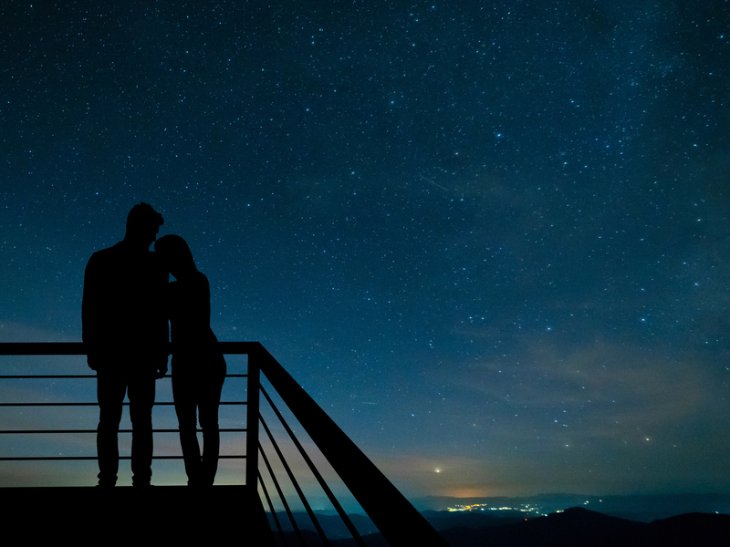 The romantic couple standing on the balcony on the scenic starry sky background