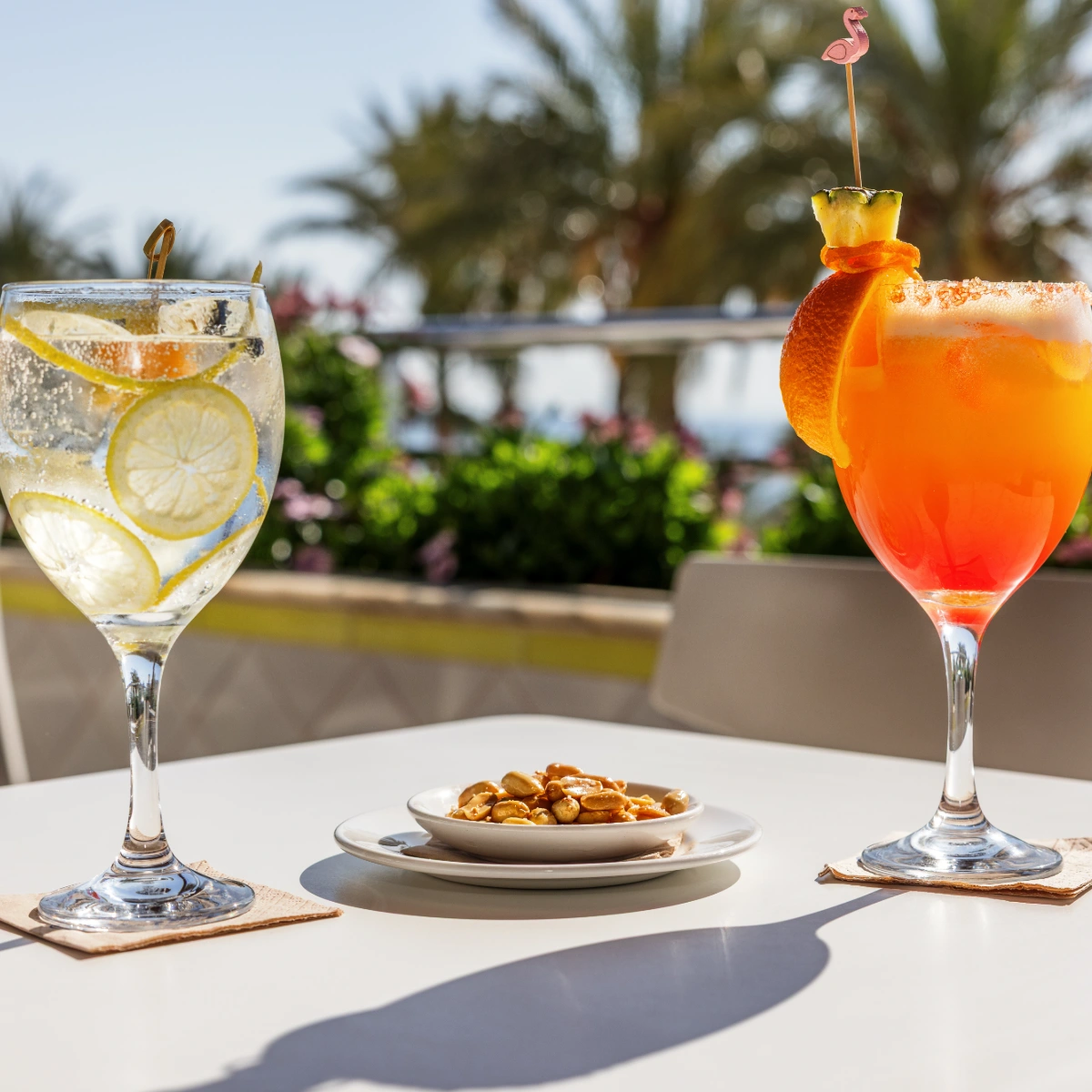 Dos c&oacute;cteles y un plato de frutos secos en una mesa al aire libre.