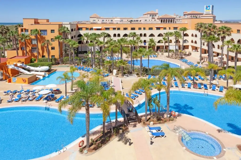 Hotel con piscina azul, palmeras y tumbonas junto al edificio en el exterior